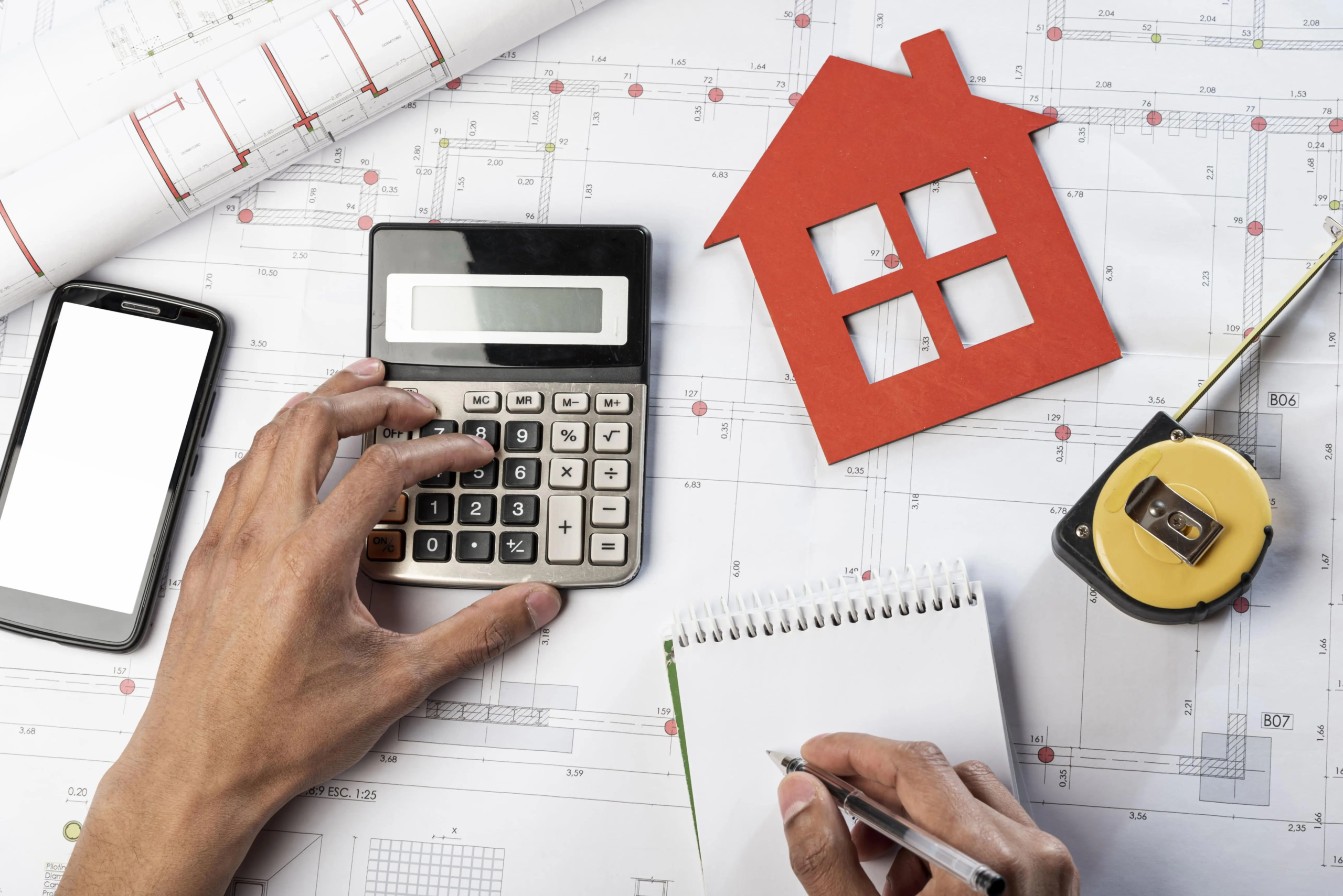 Calculator, notebook and documents arranged for planning a house purchase budget.
